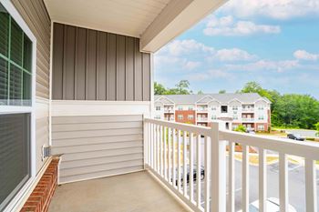 A balcony with a white railing and a view of a parking lot and buildings.